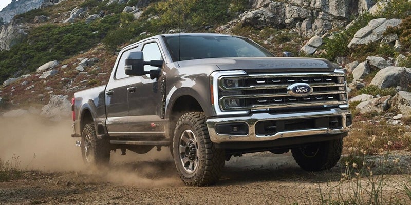 Gray Ford Super Duty pickup truck kicking up dust on a rocky dirt road with mountains in the background