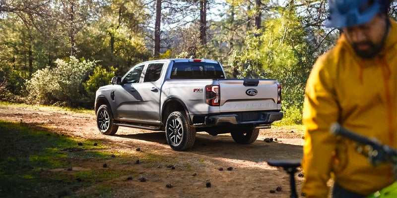 Silver Ford Ranger truck on a dirt road, driver visible in the foreground with a bike