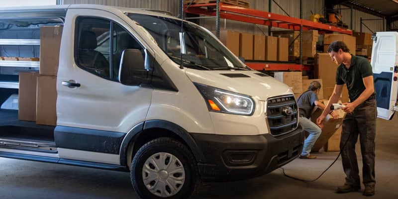 A white Ford Transit cargo van, with its side door open, being unloaded by workers in a warehouse