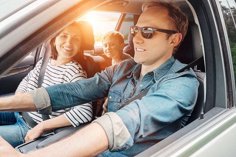 Three people seated in a car, with the driver wearing sunglasses and two passengers visible